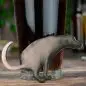 Novelty dog-shaped bottle opener leaning on a glass of dark beer on a wooden table.