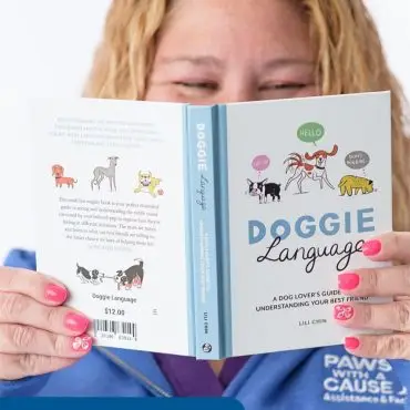 Woman reading Doggie Language book on dog body language, holding it with pink manicured nails.