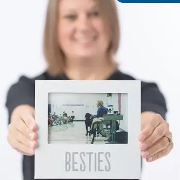 Smiling person holds framed photo labeled Besties with Libby Staff logo, showing a school presentation with a dog.