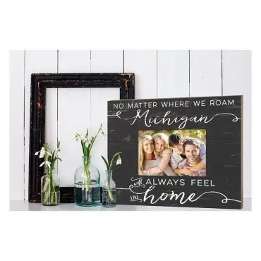 Picture frame with family photo and Michigan will always feel like home text on wooden background, next to vases.