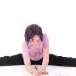 Child writing in a book while doing a split on the floor, wearing a pink shirt and black pants.