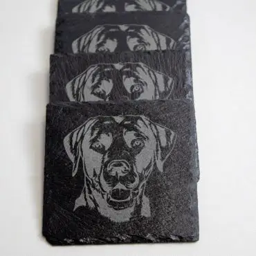 Set of black coasters featuring detailed dog engravings, perfect for pet lovers and stylish home decor.