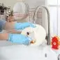 Person washing dishes at a sink with rubber gloves, using a cute animal-themed sponge.