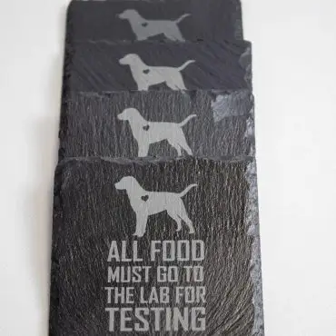 Black slate coasters with dog silhouettes and All food must go to the lab for testing text.