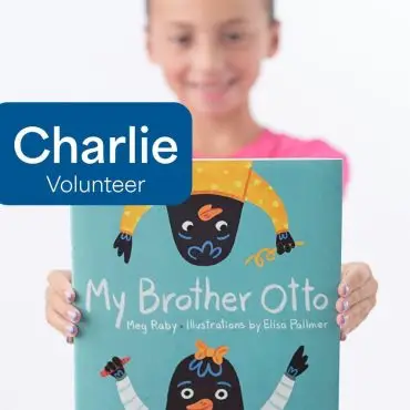 Child holding My Brother Otto book, smiling, volunteer badge with Charlie text.