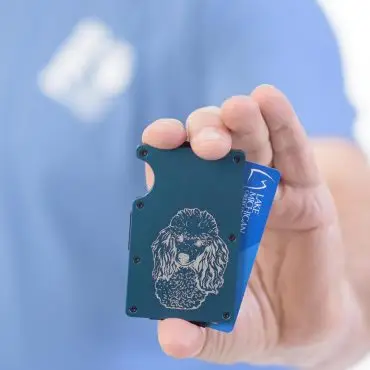 Man holding a blue minimalist wallet with poodle engraving, displaying a blue credit card partially inserted.