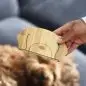 Hand holding wooden puzzle piece above blurred dog, emphasizing eco-friendly pet toys.