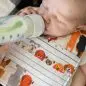 Baby drinking from a bottle wearing a colorful bib with cute dog prints.