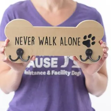 Woman holding a bone-shaped sign with Never Walk Alone text, featuring paw print design.