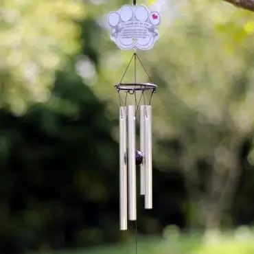 Memorial wind chime with paw print sign, hanging outdoors with blurred green background.