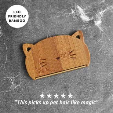 Eco-friendly bamboo pet hair remover in cat shape on fabric with loose pet hair.