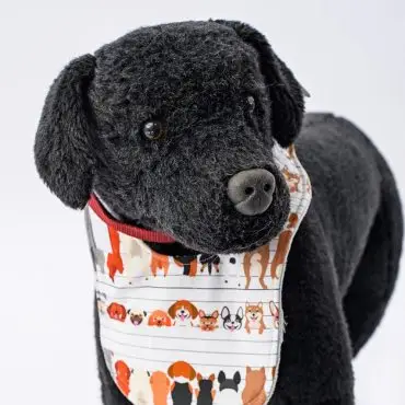 Plush black dog toy with cute dog-patterned bib on white background.