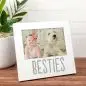 Photo frame labeled Besties with a baby and fluffy dog, sitting on a wooden table near a potted plant.