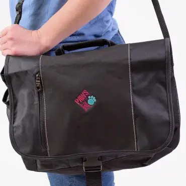 Person carrying black messenger bag with Paws logo and adjustable strap, wearing a blue shirt and jeans.