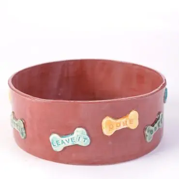 Ceramic dog bowl with colorful bone-shaped decorations and engraved commands: Sit, Stay, Come, Leave it.