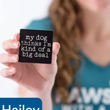 Person holding a sign that says my dog thinks I'm kind of a big deal, wearing a Paws With a Cause shirt.