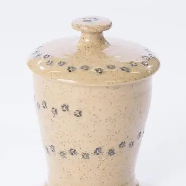 Speckled ceramic jar with paw print design and lid, beige color, isolated on white background.
