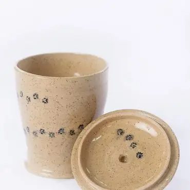 Speckled ceramic cup with lid, adorned with black paw prints, set on a white background.