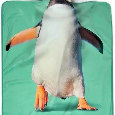 Dog posing as penguin on a green blanket, creating a humorous and playful scene.