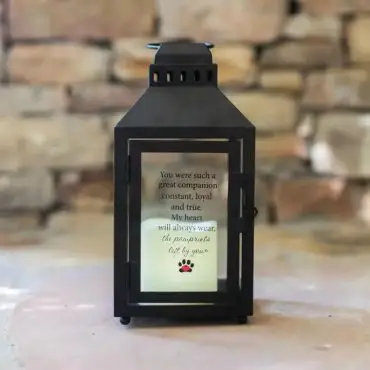Black lantern displaying a heartfelt pet memorial quote against a rustic stone background.