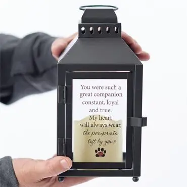 Man holding a black lantern with an engraved heartfelt message about a loyal companion and pawprints.