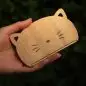 Hand holding a wooden cat-shaped phone stand against a dark green background.