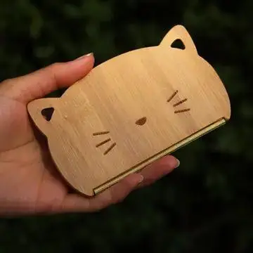 Hand holding a wooden cat-shaped phone stand against a dark green background.