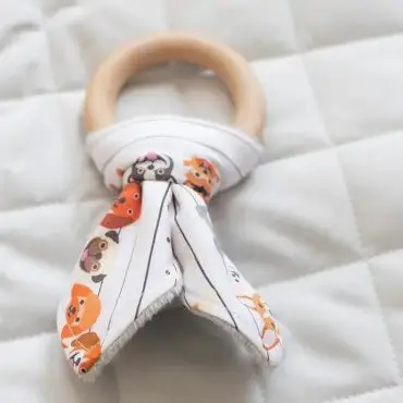 Wooden teething ring with animal-patterned fabric on a quilted background, ideal for baby care.