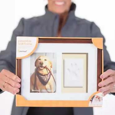 Person holding a Pawprints wall frame with a dog photo and clay paw impression, suitable for pets.