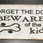 Humorous sign with text Forget the dog, beware of the kids and a bone illustration with paw prints.