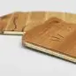 Close-up of bamboo zippered pouches with engraved initials on a plain background.