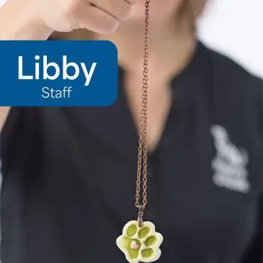 Person holding a paw-shaped necklace with a heart design, showcasing pet-themed jewelry.