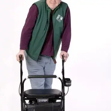 Man in hat and green vest using a U-Step walker for mobility support, white background.