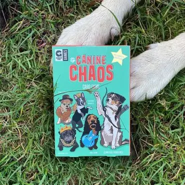 Canine Chaos card game on grass with a dog's paws nearby, featuring illustrated dogs dressed as celebrities.