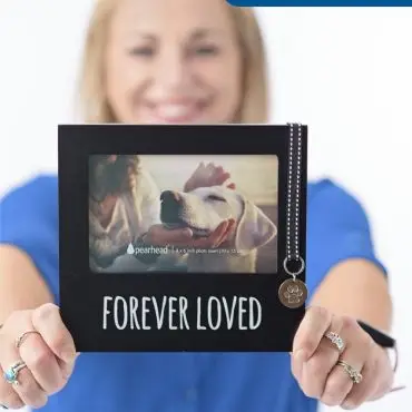 Woman holds a Forever Loved pet photo frame with a dog image, featuring a metal paw charm.