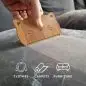 Hand holding a wooden pet hair remover tool on gray couch, effective for clothes, carpets, and furniture cleaning.