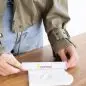Person measuring heart-shaped clay with ruler on wooden table, wearing green jacket and jeans.