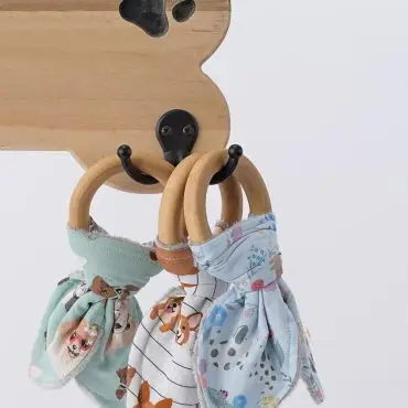 Wooden dog bone hook holding colorful baby bandana bibs with animal prints. Perfect for nursery decor or baby gifts.