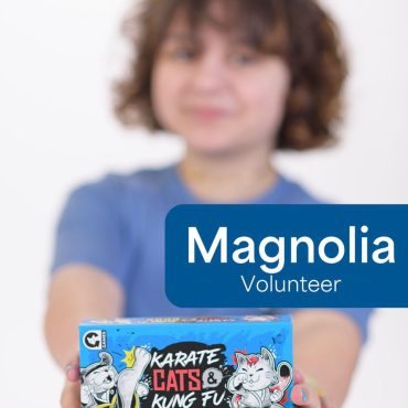 Volunteer holding Karate Cats & Kung Fu Dogs card game box, detailed with playful illustrations and colorful design.