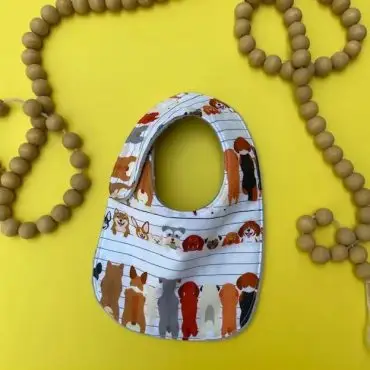 Baby bib with cute dog illustrations on a yellow background with wooden bead decor.