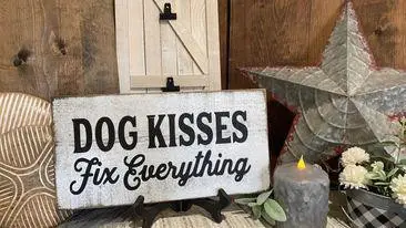 Decorative sign saying Dog Kisses Fix Everything with rustic decor, candle, and flowers on a wooden background.