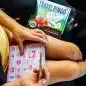 Child playing travel bingo in a car with a bingo card and pencil, enhancing road trips with fun activities.