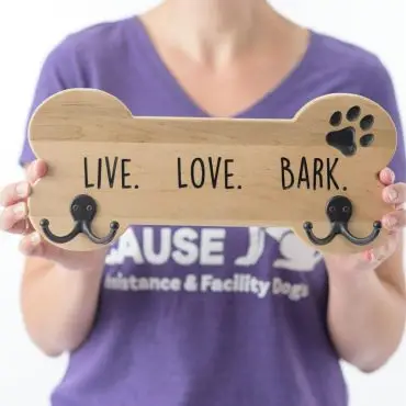 Woman holds dog bone sign with hooks and Live. Love. Bark. text, wearing a purple shirt.
