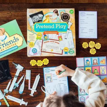 Child playing with veterinarian pretend playset, featuring pet care items and activity sheets on a wooden table.