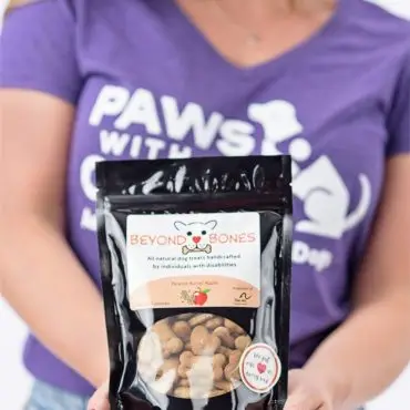 Woman holding a bag of Beyond Bones dog treats, promoting all-natural snacks made by individuals with disabilities.