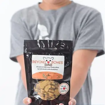Smiling child holds Beyond Bones dog treats, handcrafted by individuals with disabilities.