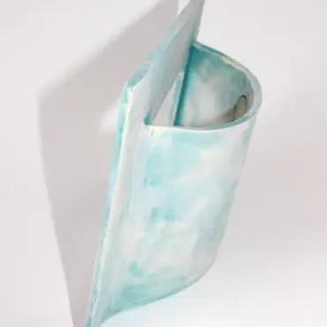 Abstract blue ceramic sculpture with curved design and textured surface, displayed against a white background.
