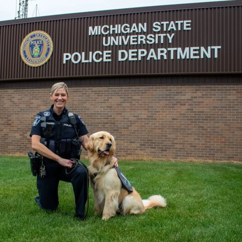 Police officer with a service dog in front of Michigan State University Police Department building.