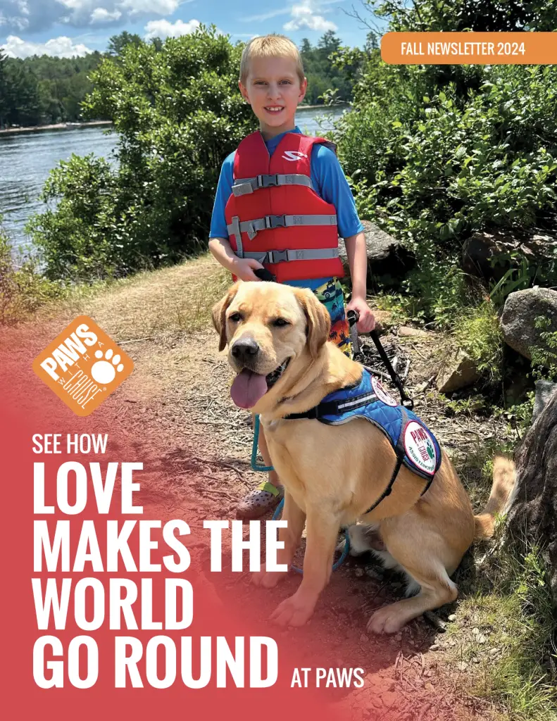 Child and service dog in life vests by a lake, promoting PAWS' mission in Fall Newsletter 2024.
