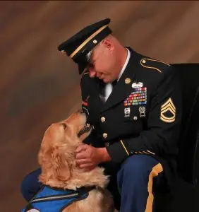 Soldier in uniform bonding with a service dog, both displaying mutual affection and companionship.